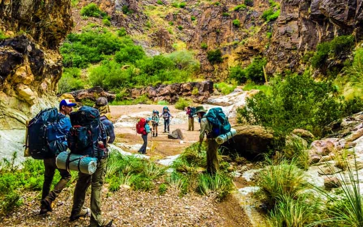 a group of gap year students carrying backpacks hike along a canyon lined greenery on an outward bound semester 